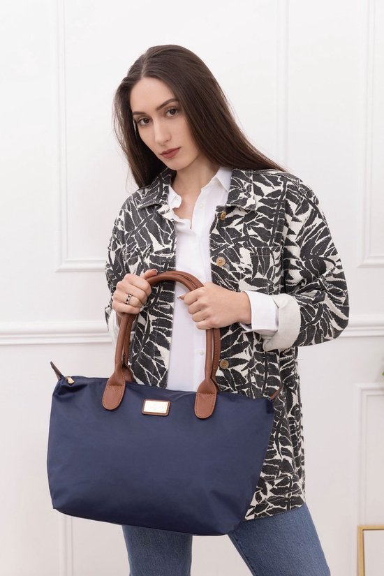 Une femme aux longs cheveux bruns tient un sac en nylon bleu foncé avec des anses en cuir marron.