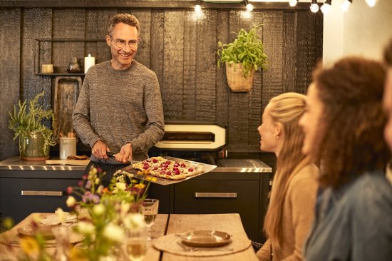 Man met grijze trui serveert pizza aan tafel.