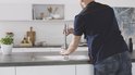 Monteur installeert chroom GROHE kraan in een moderne keuken met witte kasten en een metalen gootsteen.