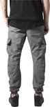 Model in grijze cargo broek met zakken en zwarte sneakers.