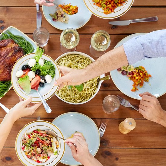 Een tafel vol eten met geroosterde kip, salade, pasta en andere gerechten. Mensen delen het eten.