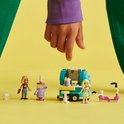 Een LEGO Friends mobiele bubbelthee stand in mintgroen en geel, met twee poppen en een roze scooter, gefilmd met een kinderhand die ernaar wijst.