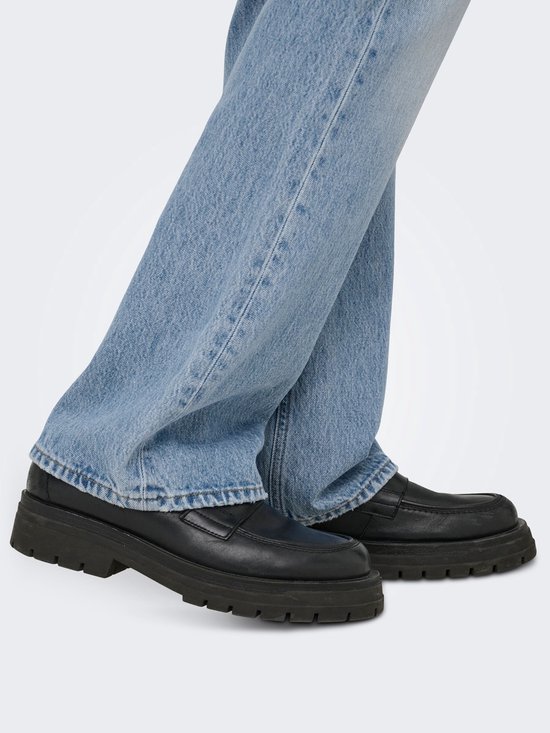 Onderlichaam van een man in lichtblauwe flared jeans en zwarte platform loafers.