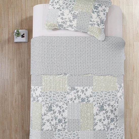 Eenpersoonsbed met blauw, groen en wit geblokte quilt met bloemen- en ruitpatronen. Kussensloop met geblokte print.
