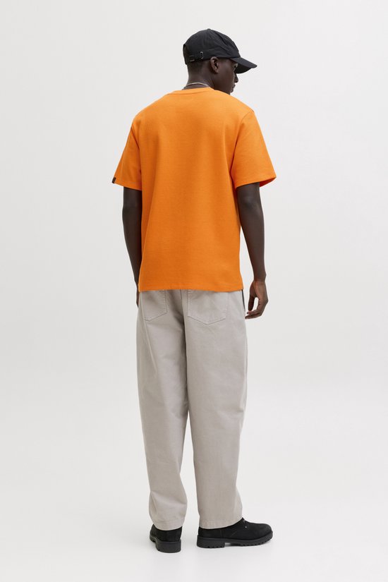 Een man draagt een oranje wafel t-shirt, beige broek en zwarte pet, van achteren gezien.