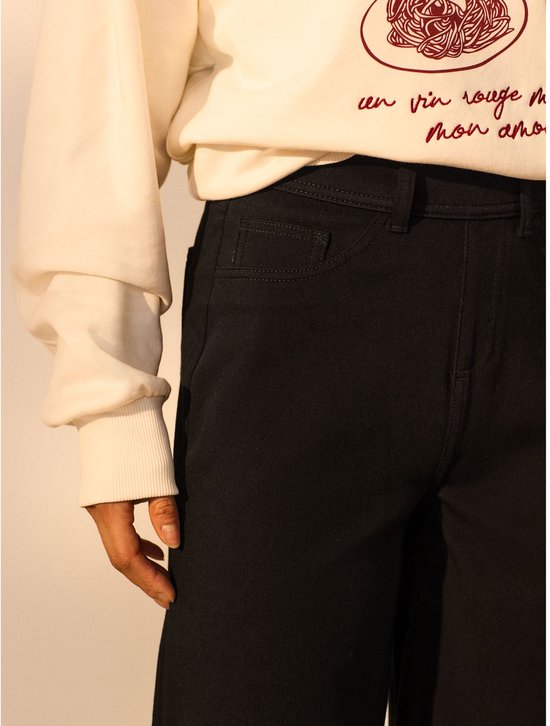Close-up van de zijkant van de zwarte jersey denim broek gedragen door een model.