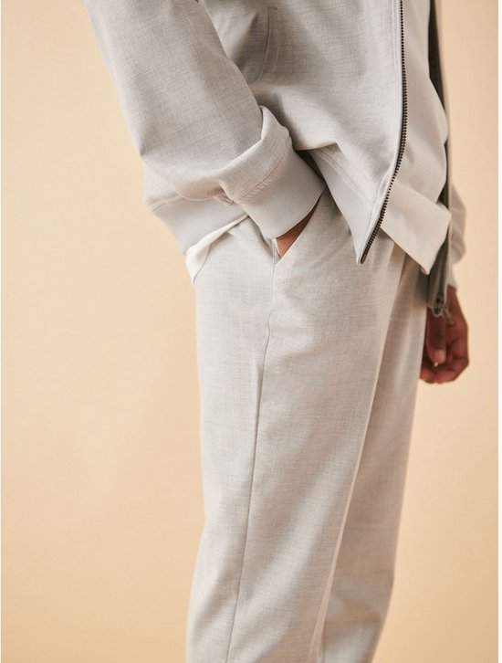 Detail van een lichtgrijze pantalon met een steekzak aan de zijkant.