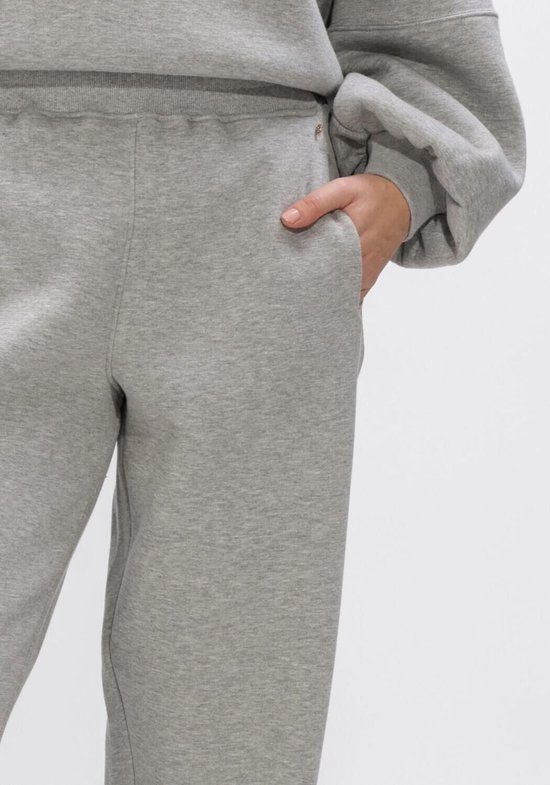 Grijze joggingbroek van dichtbij, met de hand in de steekzak.
