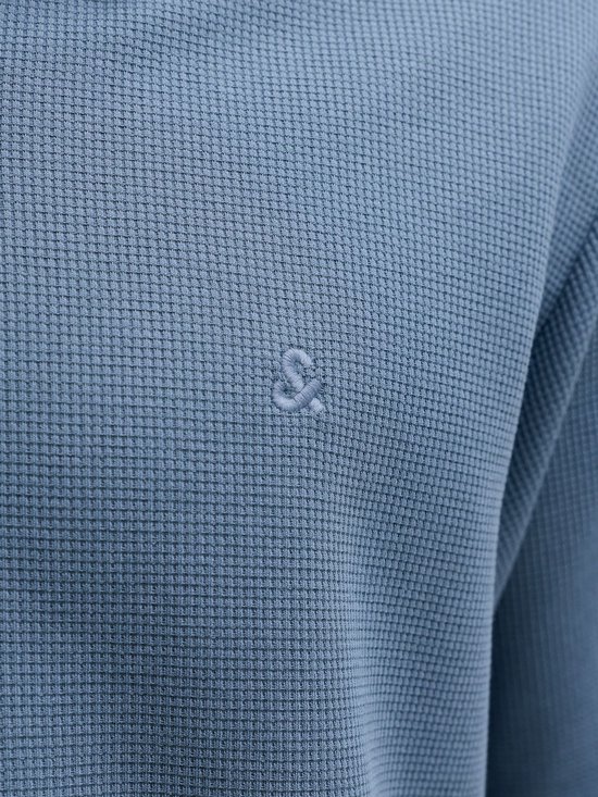 Detailopname van een blauw poloshirt met wafeltextuur en geborduurd logo.