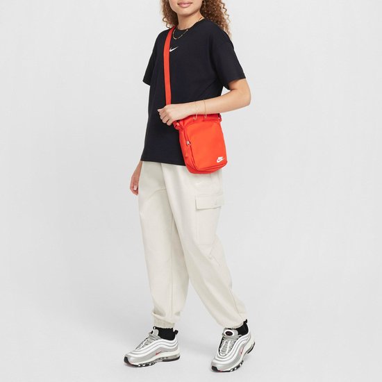 Vrouw in zwart Nike t-shirt, beige cargo broek en oranje Nike tas.