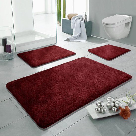 Set van drie bordeauxrode badmatten met zachte textuur in een moderne badkamer.