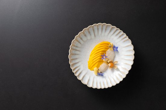 Wit dinerbord met geribbelde rand, geserveerd met mango, zoete aardappel en bloemen.