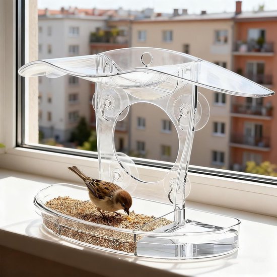 Transparant acryl vogelvoederhuisje op een vensterbank, met een mus die eet, op de achtergrond gebouwen.