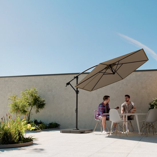 Zwarte parasolvoet met een zweefparasol in een tuin, waar twee mannen aan tafel zitten.