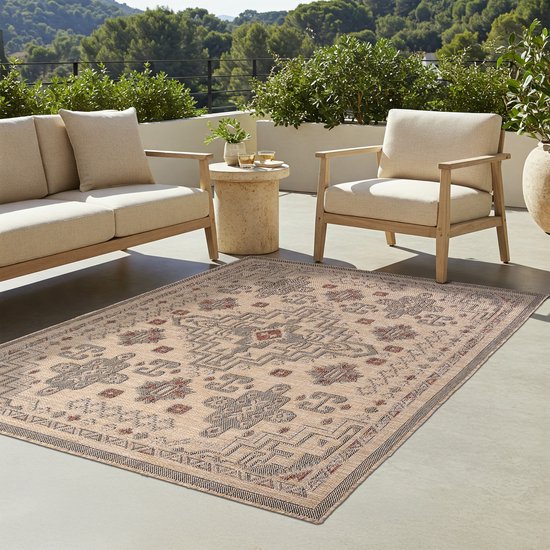 Buiten op een terras ligt een beige vloerkleed met oosters patroon, met loungebanken.