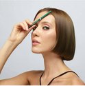 Vrouw met kort, bruin haar houdt groene eyeliner bij haar voorhoofd.