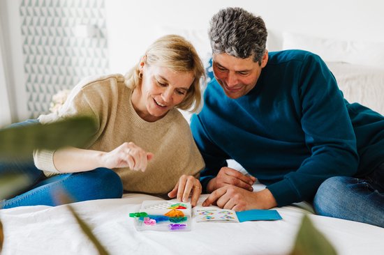 Man en vrouw die samen op een bed zitten en naar een IQ Love spel kijken, met stukken in regenboogkleuren.