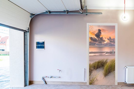 Deursticker met zonsondergang, strand en duingras, geplaatst in een garagedeur.