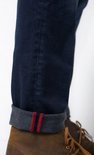 Detail van een donkerblauwe jeans met omgeslagen zoom en rode bies.