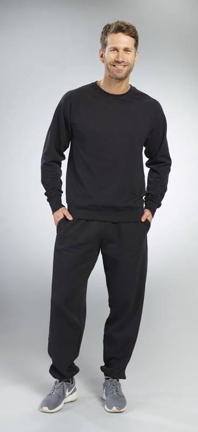 Man draagt een zwarte trui met ronde hals en een zwarte joggingbroek. Handen in de zakken.
