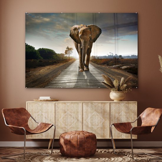 Un éléphant marche sur une route, avec un coucher de soleil et un arbre en arrière-plan.