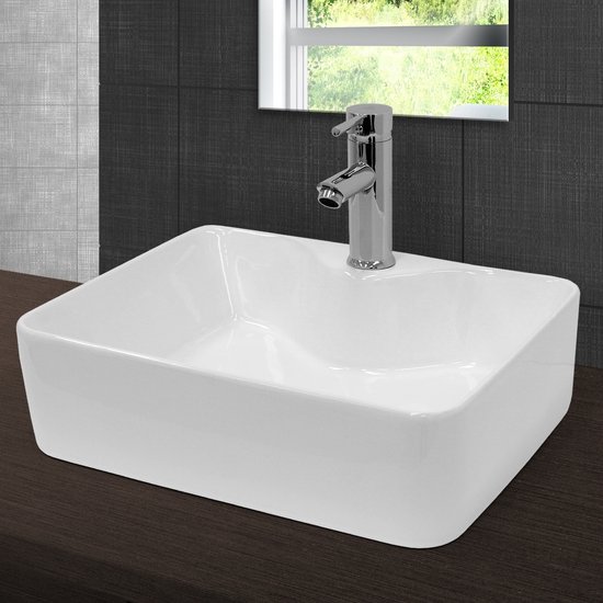 Lavabo rectangulaire en céramique blanche avec robinet chromé sur un plan de travail sombre.