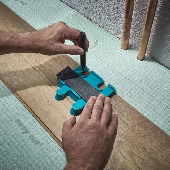 Een hand met een stift tekent een contour op een turquoise wolfcraft contourmal op een houten vloer.