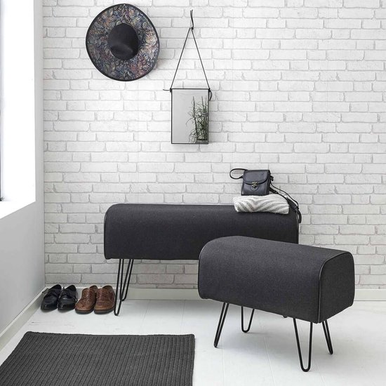 Pouffe gris foncé aux côtés arrondis et pieds compas en métal, à côté d'un pouffe plus bas.