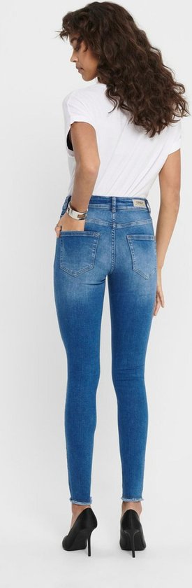 Achterkant van een vrouw in blauwe skinny jeans met rafelige zoom, gedragen met zwarte pumps.