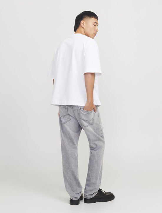 Man met witte T-shirt en grijze jeans, naar achteren gedraaid.