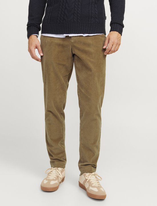 Man draagt een marineblauwe kabel gebreide trui, wit overhemd, bruine chino en beige sneakers.
