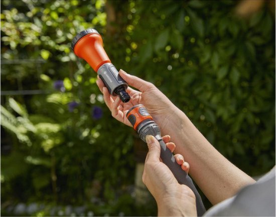 Vrouw koppelt oranje spuitmond aan tuinslang met Gardena-logo.