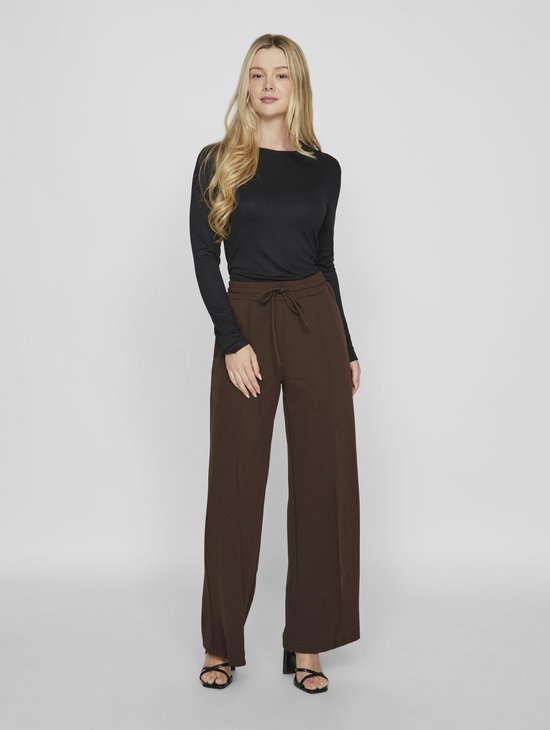 Vrouw met lange blonde haren, draagt bruine wijde broek.