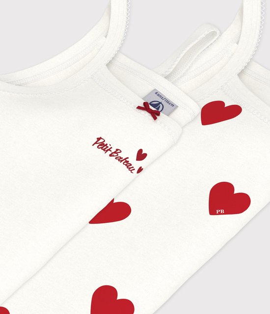 Detailopname van twee witte topjes, één met rode hartjesprint, de ander met 'Petit Bateau' opschrift en strikje.