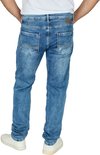 Model met blauwe jeans en witte sneakers. De jeans hebben een lichte wassing en gestikte achterzakken.