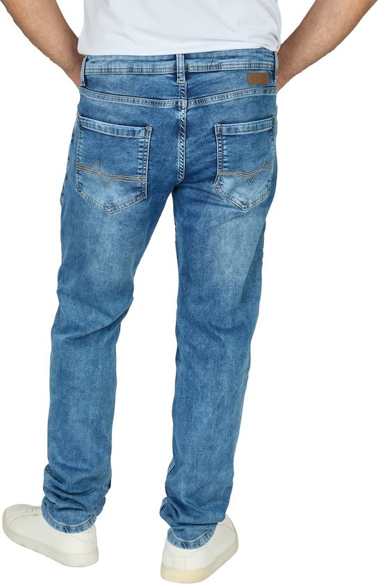 Model met blauwe jeans en witte sneakers. De jeans hebben een lichte wassing en gestikte achterzakken.