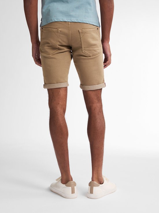 Man met bruine slim fit shorts, omgeslagen zoom en lichtblauwe sneakers, gezien vanaf de achterkant.
