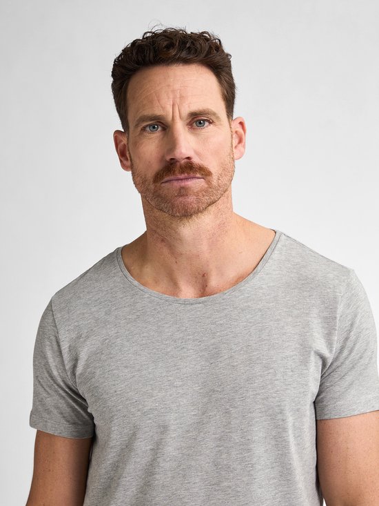 Close-up van een man met een grijs T-shirt met wijde ronde hals.