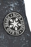 Ronde 'ROCK REBEL NEVER GIVE IN' patch met ster en schedels op een grijs jack.