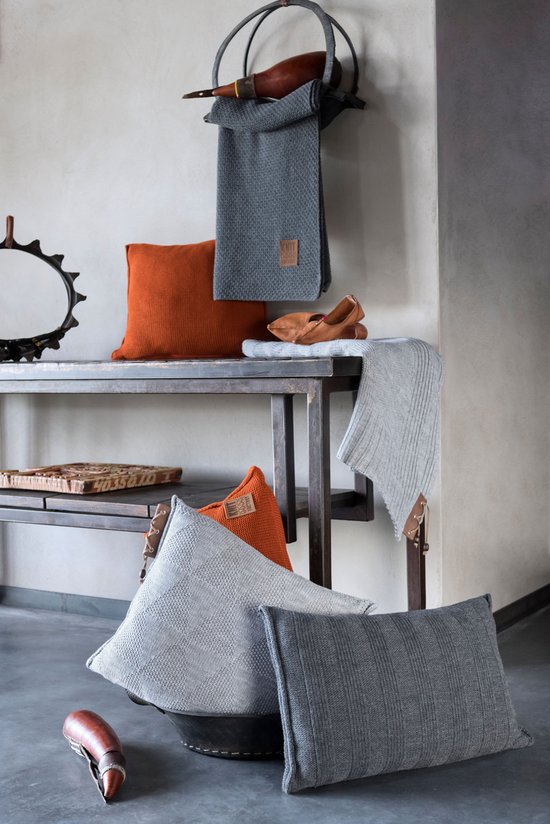 Grijze en oranje gebreide kussens en plaids op een metalen rek.
