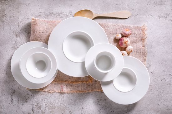 Een set witte Palmer 'White Delight' porseleinen pastaborden met een houten lepel en knoflook op een linnen onderlegger.