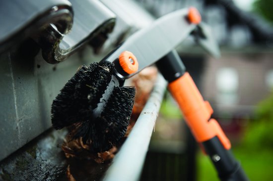 Zwarte dakgootborstel met oranje steel, in gebruik in een dakgoot.