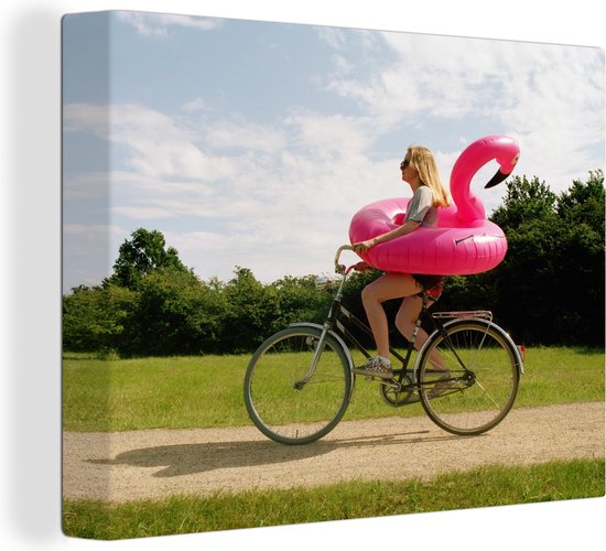 Canvas Schilderij Vrouw fietsend met een flamingo zwemband om haar heen - 120x90 cm - Wanddecoratie