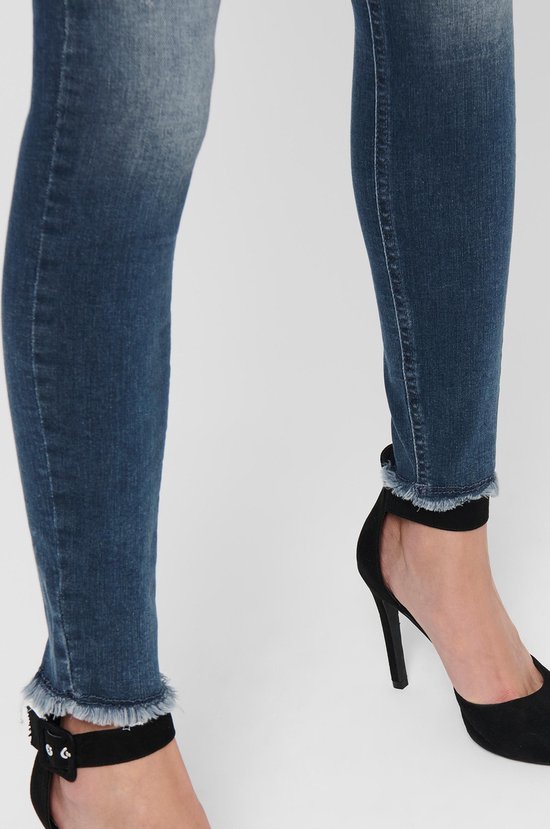 Close-up van de enkel van een vrouw in een spijkerbroek met rafelige zoom, met zwarte pumps met enkelbandje.