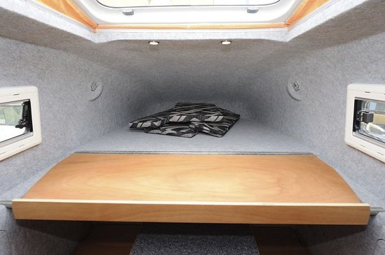 Interieur van een camper met grijs vilt beklede wanden en plafond, en een houten bed.