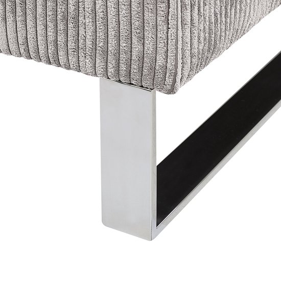 Close-up van de verchroomde metalen poot van een grijze corduroy fauteuil.