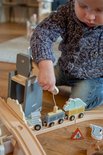 Jongen met blauwe trui speelt met houten treinbaan. Hand van de jongen bedient de kraan met een wit touw.