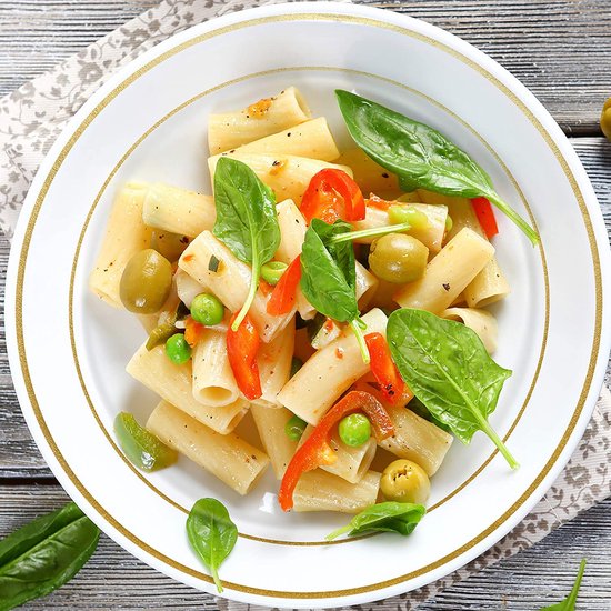 Een kom vol penne pasta met erwten, olijven, stukjes rode paprika en verse spinazie.
