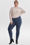 Model draagt een blauwe skinny jeans met een lichtroze trui en zwarte laarzen.