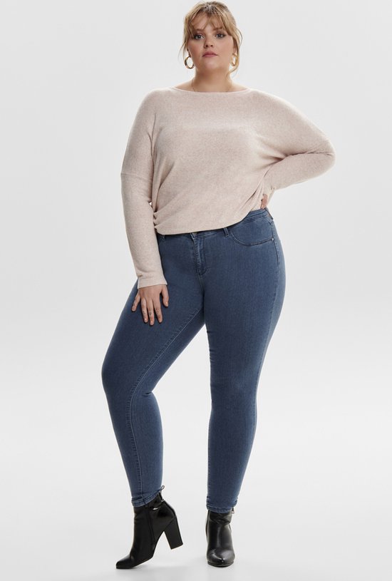 Model draagt een blauwe skinny jeans met een lichtroze trui en zwarte laarzen.